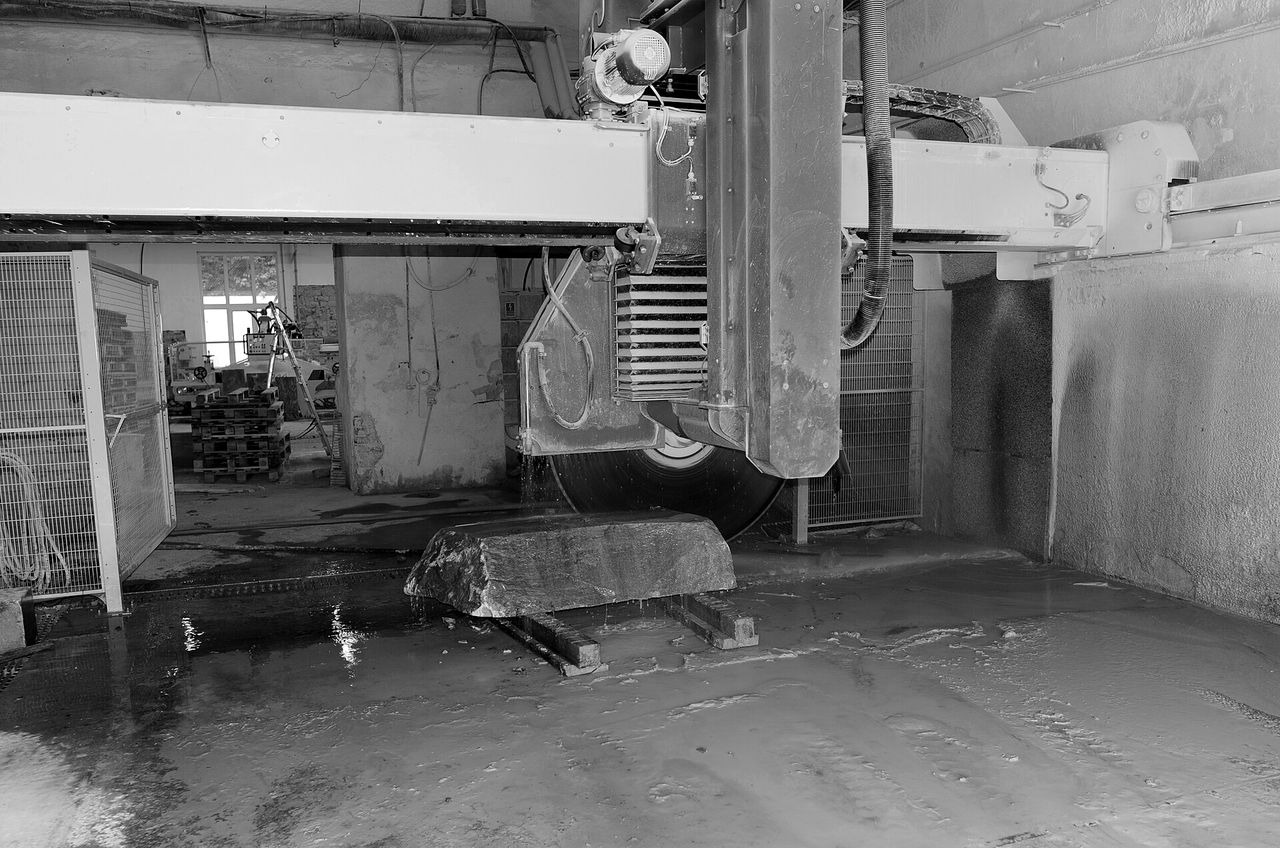 A block saw beside a marble block on a wet shop floor